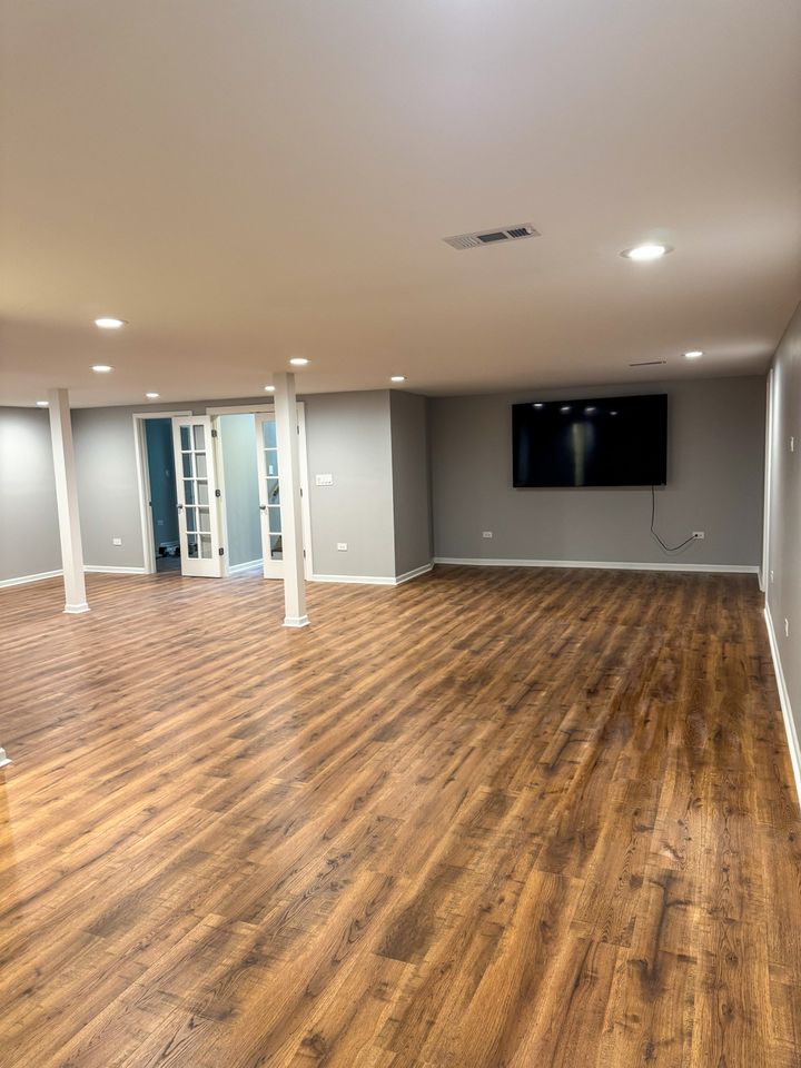 Finished basement with wood-look flooring, French doors and recessed lights